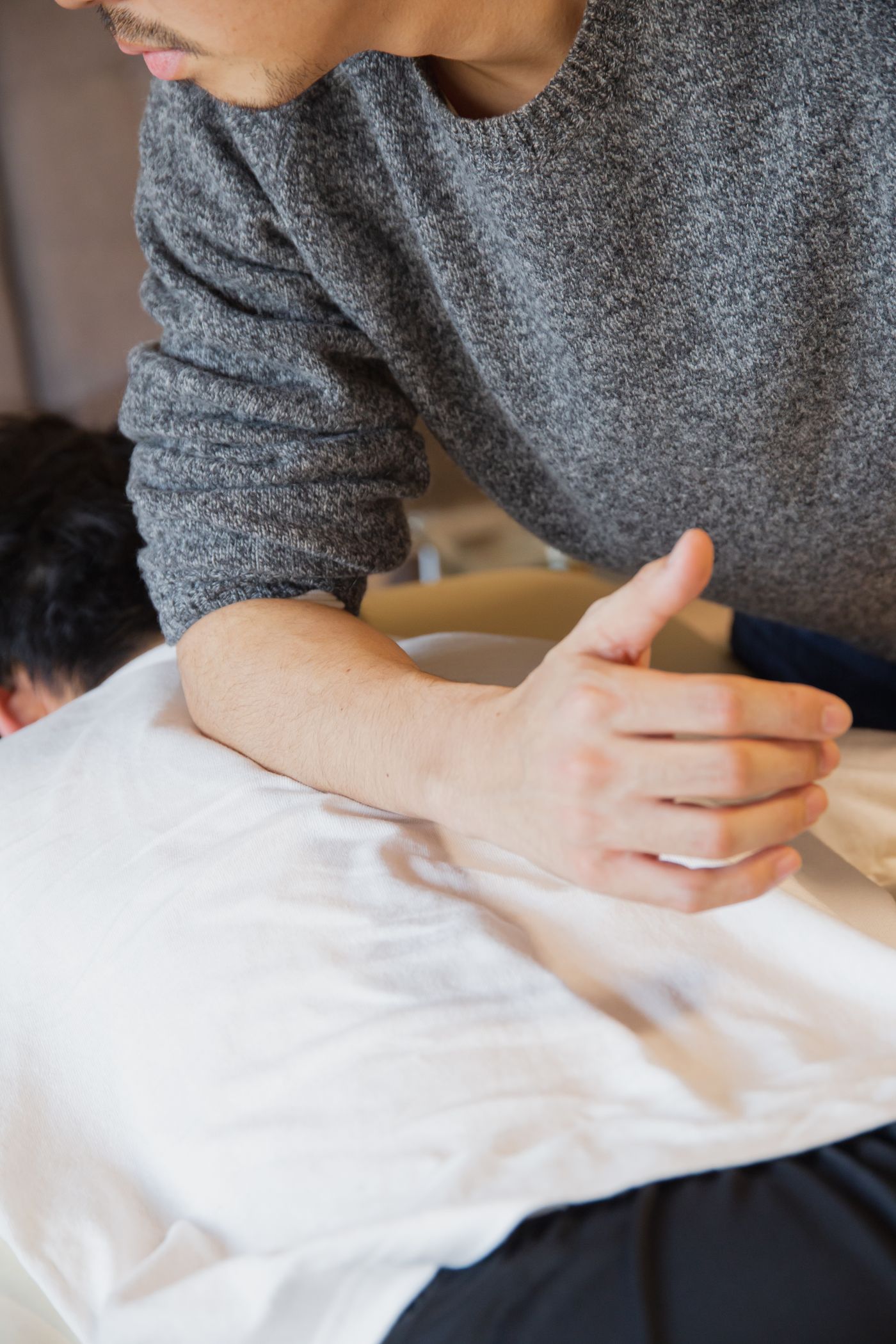 A massage therapist leaning a forearm into the muscles of a client's upper back.